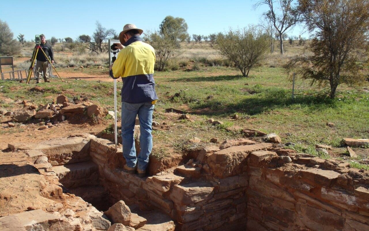 A photograph of a man holding a prismatic mirror and staff while surveying a cellar with a colleague in the background. Photo taken at the excavations at Old Owen Springs, July 2013. Image courtesy of David Steinberg